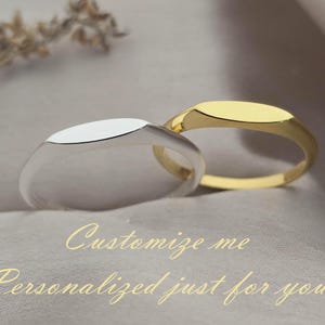 May include: Two signet rings, one silver and one gold, are displayed on a neutral background. The rings have an oval face and a smooth, polished finish. The text "Customize me, Personalized just for you" is written in cursive.