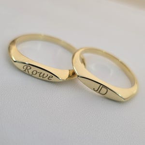 Puede incluir: Dos anillos de oro con texto grabado. Uno tiene grabado "Rowe", el otro "JD". Los anillos son de color oro brillante y tienen un acabado liso y pulido. Los anillos son probablemente para una pareja.