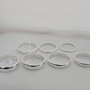 Puede incluir: Una colecci&oacute;n de siete anillos de plata de diferentes tama&ntilde;os, dispuestos sobre una superficie gris claro. Los anillos tienen un acabado liso y pulido, que refleja la luz ambiental. Los anillos probablemente son de plata de ley o un metal similar.