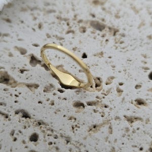 Op de afbeelding: Een gepolijste goudkleurige ring met een gladde, slanke band en een plat, langwerpig ovaalvormig oppervlak. De ring heeft een reflecterende metalen afwerking en een eenvoudig, doorlopend ontwerp dat over de gehele omtrek een constante breedte behoudt.