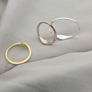 Op de afbeelding: Drie dunne metalen ringen in goud-, ros&eacute;goud- en zilverkleurige tinten. De zilveren ring is voorzien van een zichtbaar 925-keurmerk. Elke ring heeft een glad, afgerond profiel en een gepolijste afwerking, gepresenteerd als een set eenvoudige sieraden.