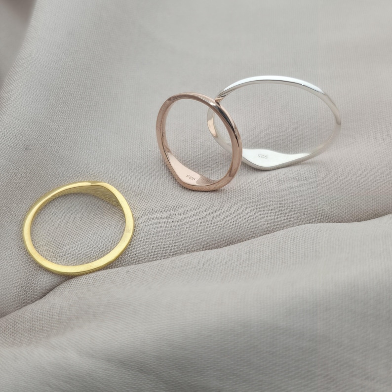 Op de afbeelding: Drie dunne metalen ringen in goud-, ros&eacute;goud- en zilverkleurige tinten. De zilveren ring is voorzien van een zichtbaar 925-keurmerk. Elke ring heeft een glad, afgerond profiel en een gepolijste afwerking, gepresenteerd als een set eenvoudige sieraden.