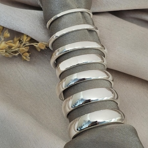 Puede incluir: Una pila de ocho servilleteros plateados brillantes. Los anillos son lisos y reflectantes, con una textura martillada en la superficie exterior. Est&aacute;n dispuestos alrededor de una servilleta gris, con un fondo beige.