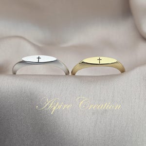 Può includere: Due anelli con sigillo con un design a croce. Uno è argentato, l'altro dorato. Ogni anello ha una faccia ovale con una croce incisa. Gli anelli sono esposti su un tessuto morbido di colore neutro.