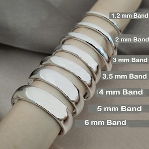 May include: A collection of polished silver bands in varying widths, from 1.2 mm to 6 mm. The bands are displayed on a neutral-toned surface, showcasing their reflective quality. The text on the image indicates the band sizes.
