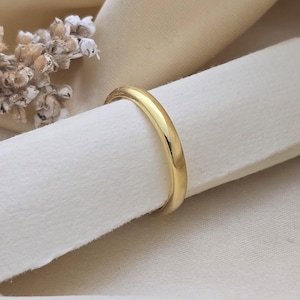 Può includere: Una fede nuziale d'oro è mostrata su una superficie bianca. L'anello ha una finitura liscia e lucida e un design classico e arrotondato. La fascia è di un caldo colore oro giallo, che riflette la luce. Lo sfondo è di una tonalità morbida e neutra, che evidenzia i dettagli dell'anello.