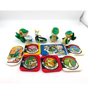 Peut inclure: Collection de jouets et de cartes Pokémon mettant en vedette le personnage Snivy. Les jouets sont verts, jaunes et blancs, et les cartes sont de couleurs variées avec du texte japonais. Les jouets sont dans différentes poses, et les cartes ont des illustrations de Snivy.