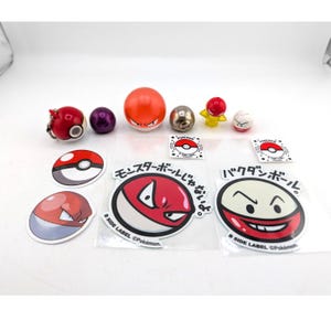 Può includere: Una collezione di vari oggetti a tema Pokémon, tra cui adesivi e giocattoli sferici. Gli adesivi presentano disegni rossi e bianchi con testo giapponese. I giocattoli sono in vari colori, tra cui rosso, arancione e argento.