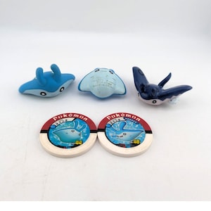 May include: A collection of Pokemon toys and game pieces. The toys include three manta ray figures in shades of blue. Two circular game pieces feature a blue manta ray graphic and the word "Pokemon".