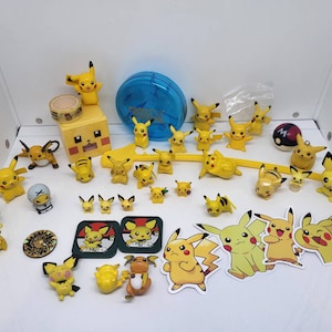 May include: A collection of yellow Pikachu figurines and stickers. The figurines vary in size and pose, with some standing, sitting, or in action poses. There's also a blue circular container and a yellow cube with a Pikachu face.