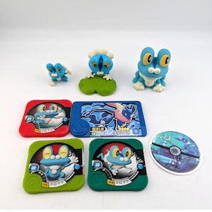 May include: Collection of Pokemon Froakie figurines and cards. The figurines are blue and white, with large yellow eyes. The cards are red, blue, green, and white, featuring Froakie and other Pokemon characters. The cards have Japanese text.