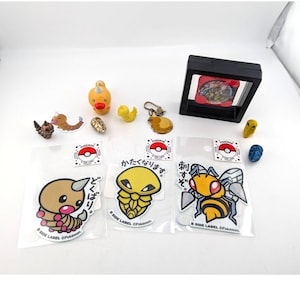 May include: A collection of Pokémon merchandise, including stickers, figurines, and a framed card. The stickers feature various Pokémon characters with Japanese text. The figurines are small and colorful, depicting different Pokémon species. The framed card is black.