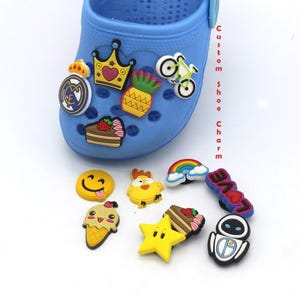 Può includere: Un set di 10 ciondoli per scarpe colorati con vari design, tra cui un ananas, una corona, una bicicletta, un viso sorridente, un pollo, un arcobaleno, una torta, una stella, un cono gelato e un robot. I ciondoli sono in gomma e sono progettati per essere attaccati alle scarpe.