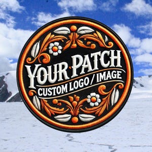 Op de afbeelding: Een ronde, zwarte geborduurde patch met een oranje rand. De patch heeft een wit bloemmotief en de tekst "YOUR PATCH CUSTOM LOGO/IMAGE".