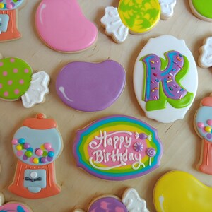 May include: Assortment of decorated sugar cookies in various shapes, including candy, gumball machines, and a cookie with the letter "K". The cookies are decorated with colorful icing and sprinkles, perfect for a birthday celebration.