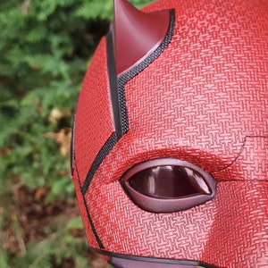 May include: Red and black Daredevil helmet with a textured surface and a single eye hole. The helmet has a pointed horn on top.