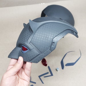 May include: A gray plastic 3D printed Daredevil helmet with red eyes. The helmet is in pieces and includes a separate top piece, horns, and eye pieces.