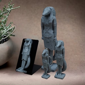 Puede incluir: Cuatro estatuas de piedra gris de una criatura mítica con cuerpo humano y cabeza de cocodrilo. Las estatuas son de diferentes tamaños y están dispuestas en fila sobre una superficie marrón.