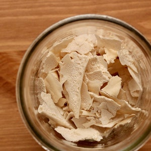 May include: A glass jar filled with white, dried, flaky pieces of yeast.