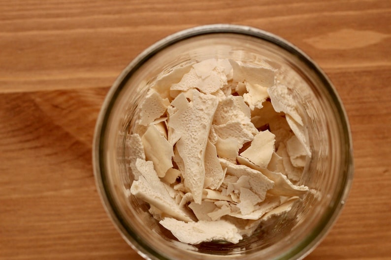 May include: A glass jar filled with white, dried, flaky pieces of yeast.