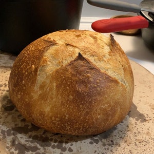 May include: A freshly baked loaf of sourdough bread with a golden brown crust and a slightly cracked surface.