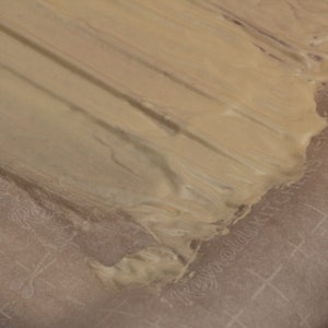 May include: A close-up of a light brown substance spread on a white parchment paper with a grid pattern.