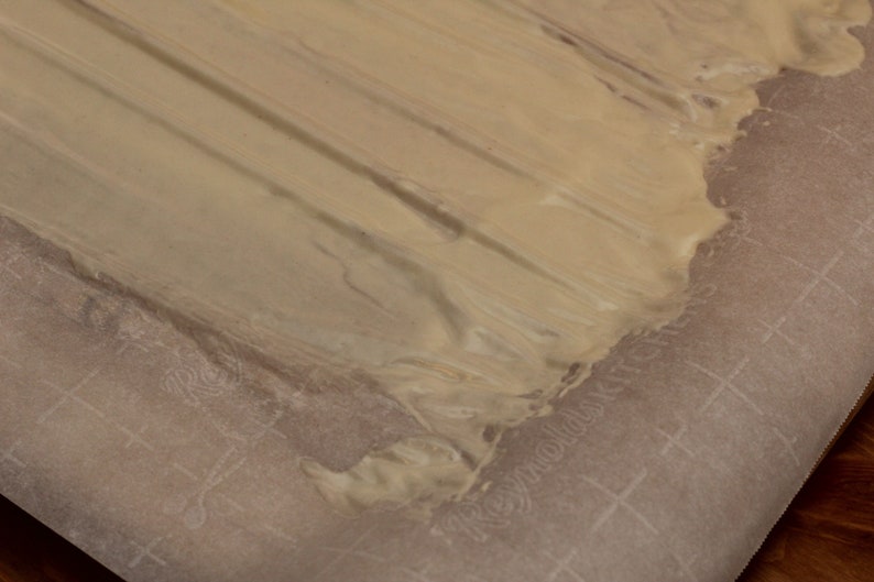 May include: A close-up of a light brown substance spread on a white parchment paper with a grid pattern.