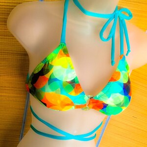 May include: A turquoise and multi-colored bikini with a geometric pattern. The bikini top has a halter style with a turquoise tie at the neck. The bikini bottom has a low-rise cut with turquoise ties on the sides.
