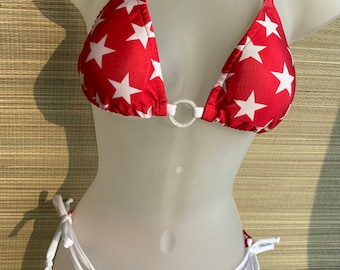 May include: Red and white star print bikini top with a white string tie and a silver ring in the center. The matching bikini bottom is blue and white striped with white string ties.