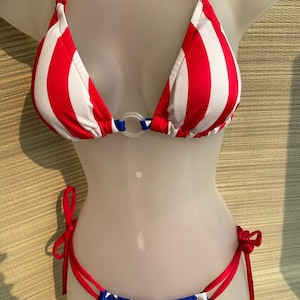 May include: Red, white, and blue striped bikini top with a ring detail. The matching bikini bottom is blue with white stars.
