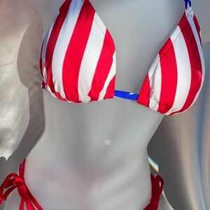 May include: A two-piece bikini set featuring a triangle top with vertical red and white stripes and blue halter straps. The matching bikini bottom features a blue base with white stars and red side ties for an adjustable fit on each hip.