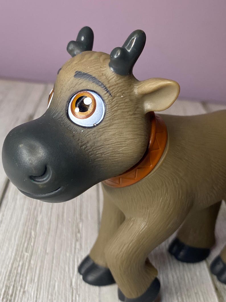 K&ouml;nnte beinhalten: Ein braunes Spielzeugrentier mit gro&szlig;en, ausdrucksstarken Augen und dunkelgrauen Geweihen. Das Rentier hat eine schwarze Nase und einen orangefarbenen Kragen. Das Spielzeug besteht aus Kunststoff und hat eine detaillierte, strukturierte Oberfl&auml;che.