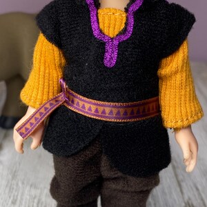 K&ouml;nnte beinhalten: Puppe in einem Kost&uuml;m mit schwarzer Weste, gelben &Auml;rmeln und brauner Hose. Die Weste hat eine lila Verzierung und einen passenden G&uuml;rtel. Das Outfit der Puppe erinnert an eine Figur aus einem beliebten Animationsfilm.