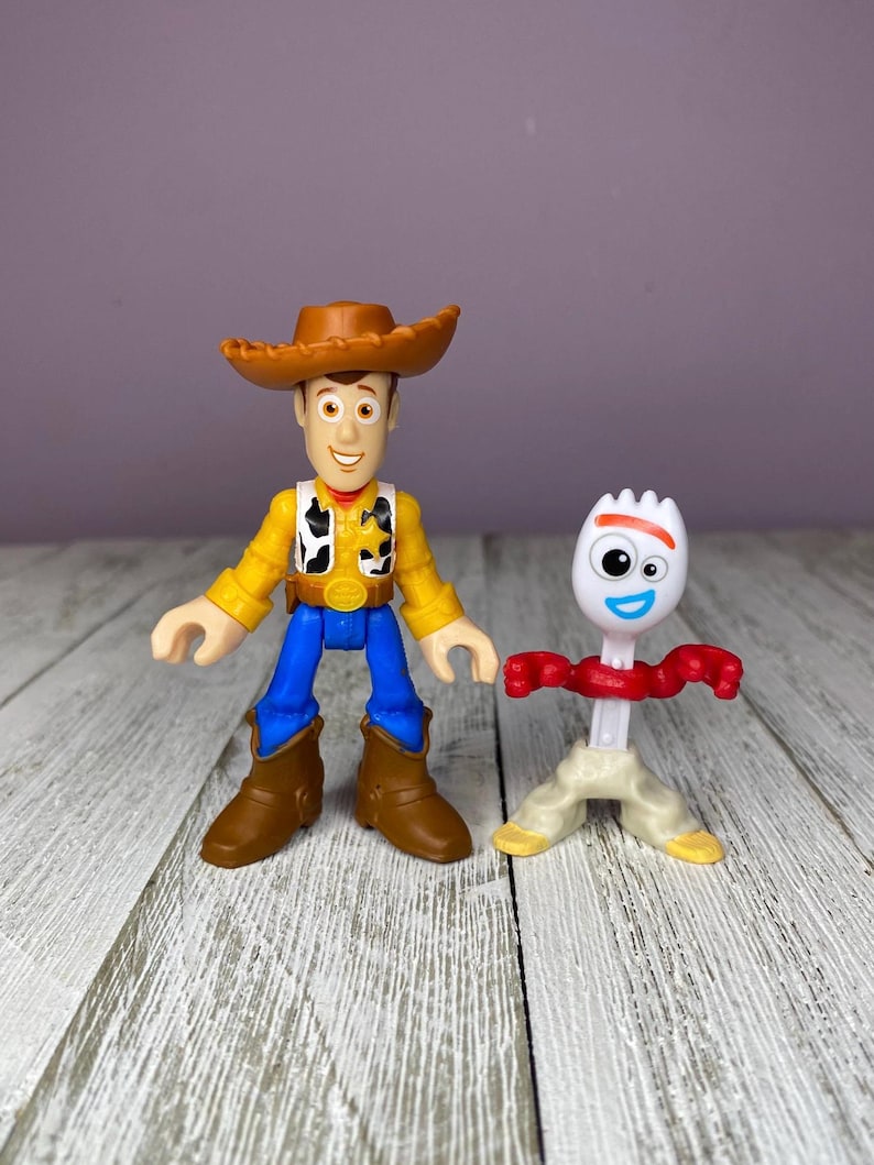 May include: Two plastic toy figures from the animated film Toy Story. One figure is Woody, a cowboy with a brown hat, yellow shirt, blue pants, and brown boots. The other is Forky, a white spork with red arms and a smiling face.