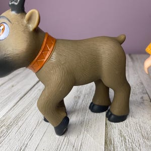 K&ouml;nnte beinhalten: Ein braunes Spielzeug-Rentier mit beigem K&ouml;rper, schwarzen Hufen und einem orangefarbenen Halsband. Das Rentier hat gro&szlig;e Augen und schwarzes Geweih. Das Spielzeug steht auf einer wei&szlig;en Holzoberfl&auml;che.