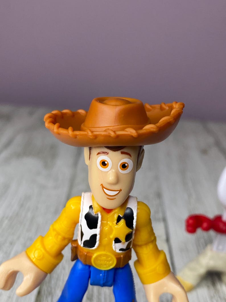 May include: A Woody action figure from the Toy Story franchise. The figure has a brown cowboy hat, a yellow shirt, a black and white vest, blue pants, and a sheriff's badge. The figure is made of plastic and is a collectible item.