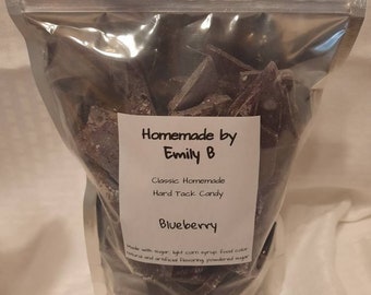 May include: A clear plastic bag filled with dark purple hard tack candy. The label reads "Homemade by Emily B" and "Blueberry." The candy pieces are irregularly shaped. The ingredients include sugar, corn syrup, and flavoring.