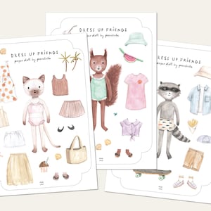 Könnte beinhalten: Drei illustrierte Papierbögen mit dem Text "DRESS UP FRIENDS" zeigen Tierfiguren und Kleidung. Eine Katze, ein Eichhörnchen und ein Waschbär sind mit Outfits wie Kleidern, Röcken, Hemden und Accessoires dargestellt. Die Illustrationen sind in sanften Aquarelltönen gehalten.