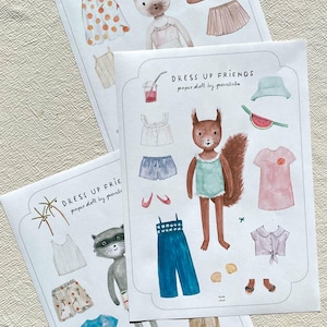 May include: Three paper doll sets with illustrations of animals and clothing. The sets include a cat, squirrel, and raccoon with outfits like dresses, shorts, and tops. The text "DRESS UP FRIENDS paper doll by povalala" is printed on each set.