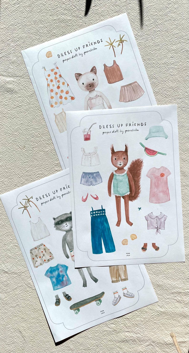 May include: Three paper doll sets with illustrations of animals and clothing. The sets include a cat, squirrel, and raccoon with outfits like dresses, shorts, and tops. The text "DRESS UP FRIENDS paper doll by povalala" is printed on each set.