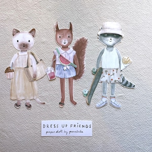 May include: Watercolor paper dolls of three animal characters: a cat, a squirrel, and a raccoon. The cat holds a cupcake and a tote bag. The squirrel has a watermelon fanny pack. The raccoon has a skateboard. The text reads "DRESS UP FRIENDS paper doll by poralala."