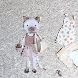 May include: Watercolor illustration of a cat character holding a cupcake and a tote bag, wearing a pink skirt and flats. Additional clothing items include a dress with orange fruit designs, a tan cardigan, and a light blue shirt.