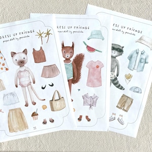 May include: Three paper doll sets with animal characters and clothing. The sets include a cat, squirrel, and raccoon, each with outfits like dresses, skirts, shirts, and accessories. The text "DRESS UP FRIENDS" is at the top of each set.