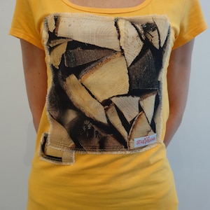 Op de afbeelding: Een felgeel T-shirt met korte mouwen en een grote, rechthoekige opgestikte lap met een fotoprint van gestapeld brandhout. De lap heeft gerafelde randen en bevat een klein wit label met de rode tekst ELEVIENNA.