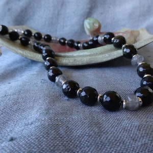 Könnte beinhalten: Eine schwarze und silberne Perlenkette mit einem silbernen Verschluss. Die Kette besteht aus facettierten schwarzen Onyx- und klaren Labradoritperlen.