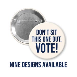 May include: A round pin-back button with a cream-colored front featuring the dark blue text DON'T SIT THIS ONE OUT. VOTE! The back of the button is metallic silver with a horizontal pin mechanism. The text NINE DESIGNS AVAILABLE is below.