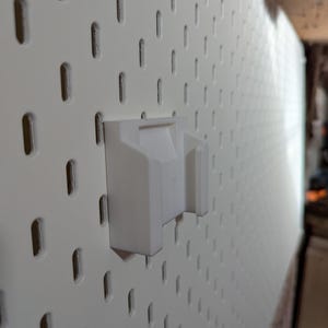 May include: A white pegboard with a white plastic holder attached. The pegboard has evenly spaced, vertical slots. The holder is designed to fit into the slots, providing a mounting point for tools or other items.