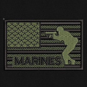 May include: Green embroidered patch with an American flag design and a silhouette of a soldier holding a rifle. The text "MARINES" is below the flag.