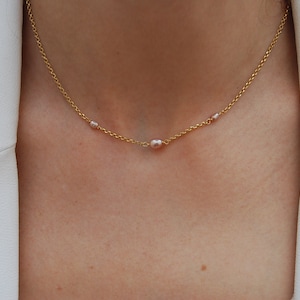 May include: A delicate gold chain necklace with three small pink pearls.