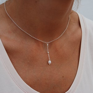 Puede incluir: Un delicado collar de cadena de plata con un solo colgante de perla. La cadena es simple, fina y la perla es peque&ntilde;a y blanca.